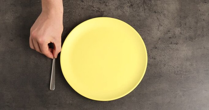 Man putting plate and cutlery onto grey table, top view