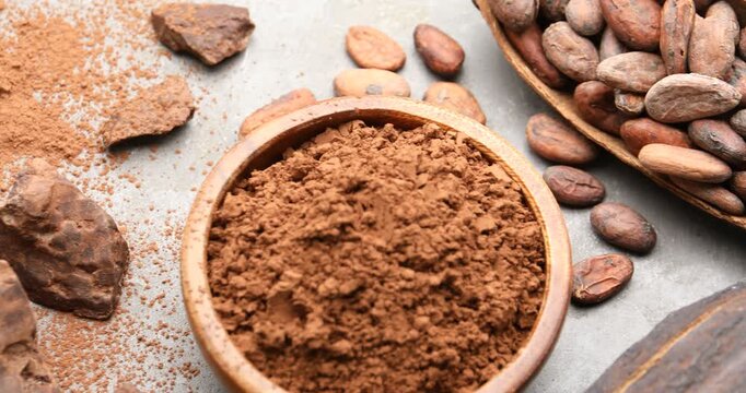 Cocoa powder, beans, pods and pieces of chocolate on grey table, top view. Camera moving right