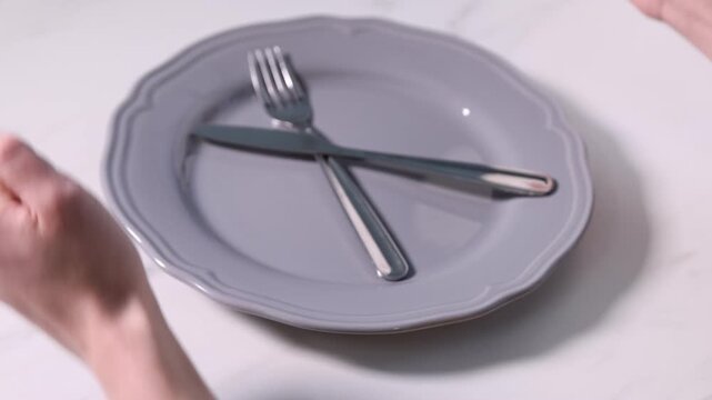 Woman making fists at white table with plate and cutlery, closeup