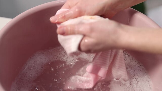 Woman washing stained kid's shirt in basinet at home, closeup