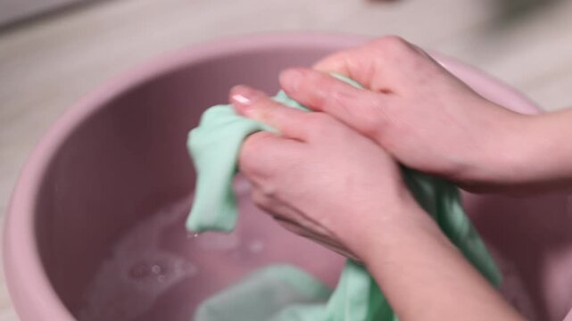 Woman washing stained kid's shirt in basinet at home, closeup