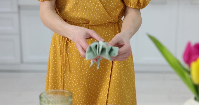 Beautiful place setting. Woman folding napkin with ring at table in kitchen, closeup. Camera moving down and forward