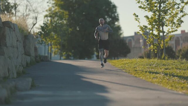 Tattooed man jogging towards camera in sunny park