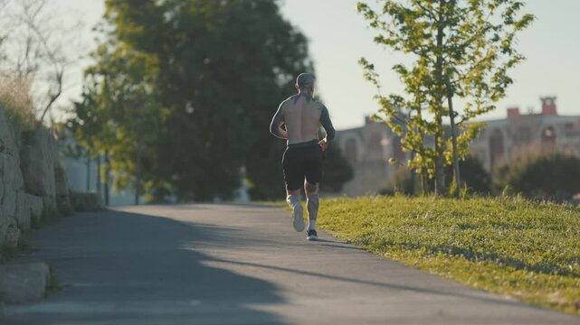 Shirtless tattooed man running in park during sunset