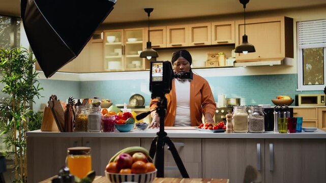 Behind the scenes, food vlog, woman recording, camera on tripod, making a recipe development and showing the cooking process for online platforms. Female home chef at kitchen counter.