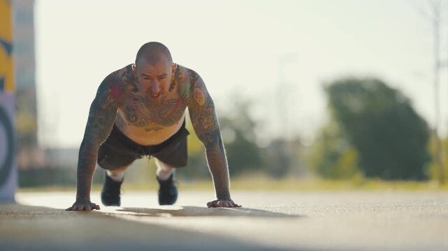 Strong tattooed man doing push-ups outdoors