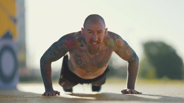 Tattooed muscular man doing push-ups outdoor workout
