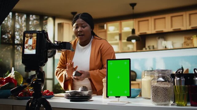 Vertical tablet, green screen, african american influencer, filming food vlog, making a recipe and showing meal prep for online audience. Recording culinary content, behind the scenes.