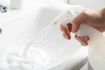 Naklejka premium Hand spraying white cleaning foam from a plastic bottle into a bathroom sink