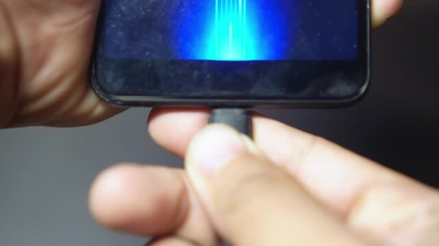 Close-up of a hand plugging a charger into a smartphone, showing the process of charging a mobile device. This scene represents modern technology, battery power, energy, and everyday digital lifestyle