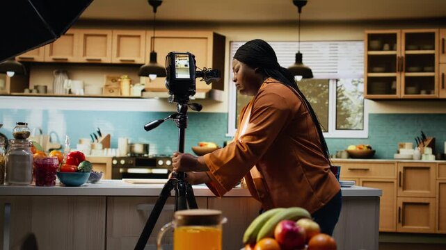 Behind the scenes, black home chef, filming setup, before recording, food vlog, content creator positioning the camera and tripod, testing natural light and video settings in the kitchen,