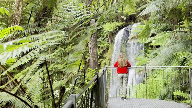 Adventurer girl stands on the viewing platform and admires the powerful Beauchamp Falls in Great Otway National Park, Victoria, Australia, one of the beautiful waterfalls located near Melbourne
