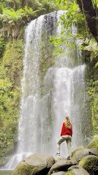 Girl adventurer stands on rock and admires the powerful Beauchamp Falls, surrounded by lush vegetation, located in Great Otway National Park, Victoria, Australia. Stunning waterfalls in the Otways reg