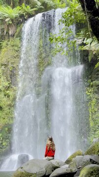 Adventurer girl sits on the rock close to and admires the powerful Beauchamp Falls in Great Otway National Park, Victoria, Australia, most beautiful waterfalls located near Melbourne