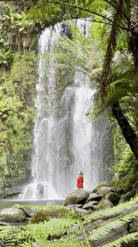 Girl adventurer stands on rock and admires the powerful Beauchamp Falls, surrounded by lush vegetation, located in Great Otway National Park, Victoria, Australia. Stunning waterfalls in the Otways reg