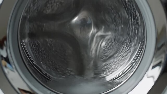 Water pouring into modern washing machine drum with detergent