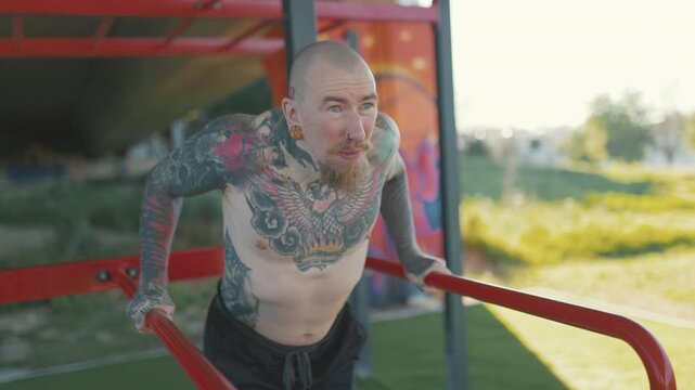 Tattooed muscular man exercising dips on parallel bars