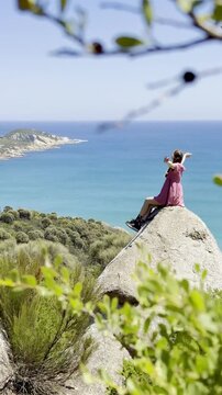 Girl adventurer sits on a large rock with her arms spread, admiring the stunning view over Fairy Cove and the turquoise ocean in Wilsons Promontory National Park, Victoria, Australia