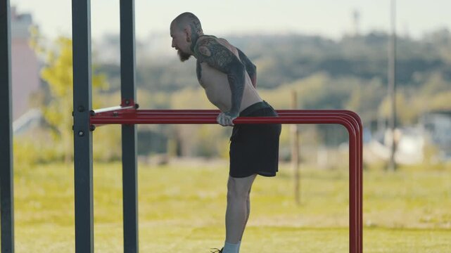 Tattooed athletic man performing triceps dips on parallel bars