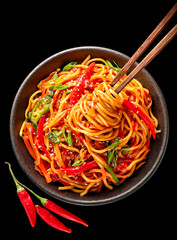 A delicious bowl of asian noodles with red chili peppers and chopsticks on a black background in a studio shot