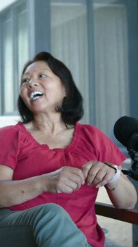 Vertical video: Recording starting woman in red blouse miming driving checking watch at home by mic