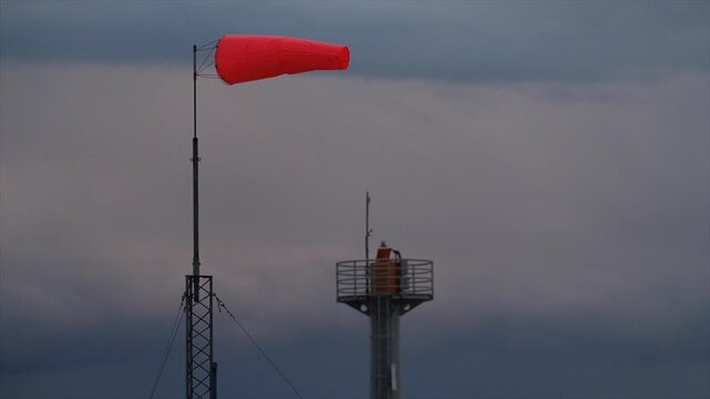 Red windsock blowing in strong wind against stormy sky
