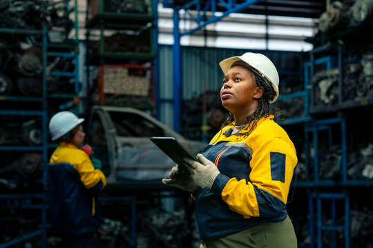 Female warehouse worker engineer using digital tablet inspecting spare parts and industrial factory storage, inventory management and maintenance workflow in automotive workshop and quality control.