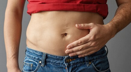 Naklejka premium Close up of a man pressing his hand against his bare stomach. Male midsection with red shirt pulled up. Healthcare concept for digestive pain, bloating or weight management