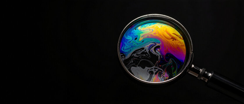 Optical lens focus on chromatic liquid pattern. Close up view of metal frame instrument for science experiment visualization or digital art texture project.