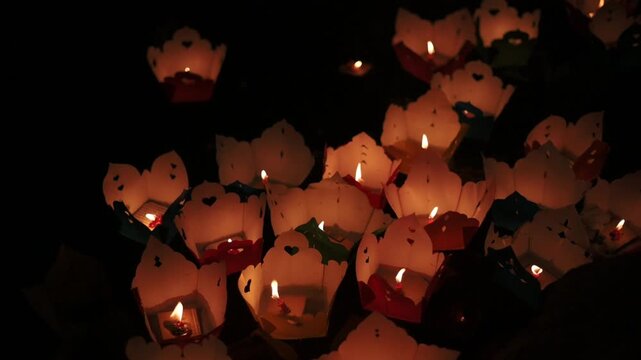 Intimate Lotus Lanterns Lit On River In Hoi An, Small Candle Flames Visible Inside Delicate Paper Bowls, Quiet Devotional Mood, Soft Orange Highlights And Reflective Water Surface