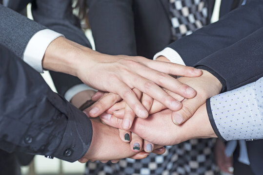Diverse business professionals stacking hands together in unity, symbolizing teamwork, collaboration, and successful partnership in corporate environment.