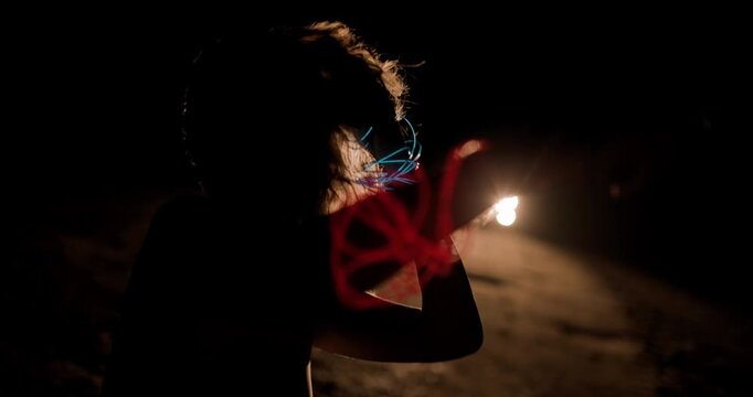 Girl dancing in silhouette illuminated by car headlights at night near an empty road, showcasing movements and shadows