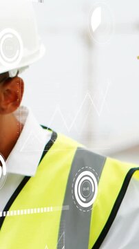 Vertical video: Construction lead studying tablet monitoring site HUD tracking turn moving by crane