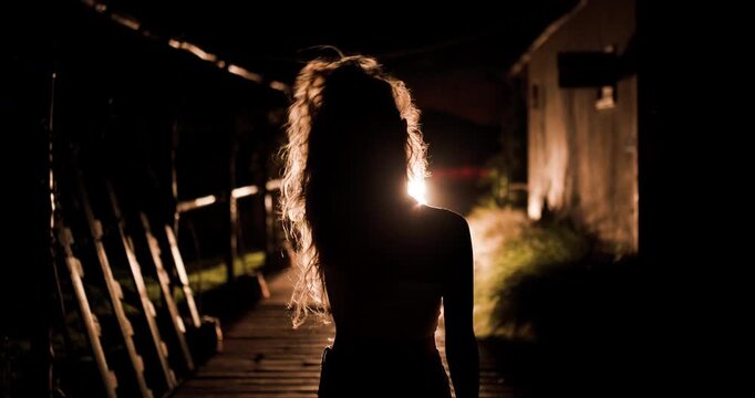 Girl walks along a dark path illuminated by car headlights during a quiet evening stroll in a secluded area