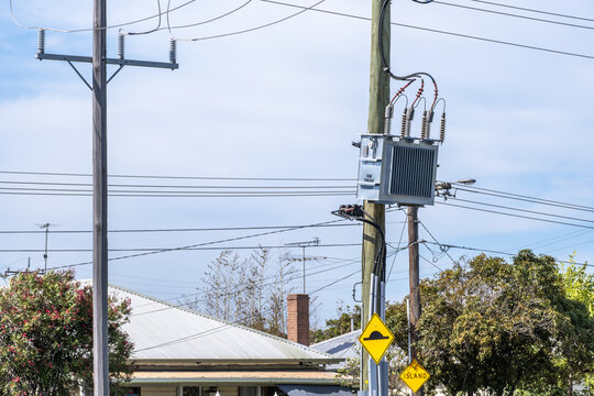 Electricity distribution transformer mounted on a utility pole in a suburban neighborhood in Australia, with overhead power lines and residential houses nearby. Urban infrastructure, energy supply