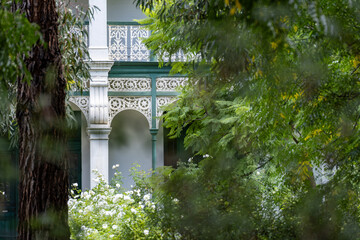 Naklejka premium Elegant heritage house behind lush greenery in Melbourne, Australia, featuring ornate veranda and a private garden. Upscale residential property, leafy exclusive environment and historic architecture 