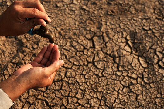 Water scarcity concept: Filling Plastic Bottle from Faucet in Dry Cracked Land at Sunset