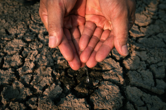 Hand catching scarce water drops over severely cracked drought soil under extreme dryness.