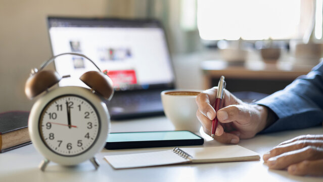 close up shot, hand of businessman taking diary work in note pad with coffee cup and laptop on desk before taking a break at lunch time