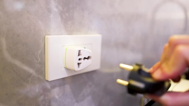 Hand Unplugging a Black Power Cord from a European Wall Socket