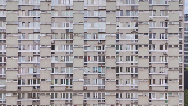 4K repetitive, high-density grid of windows and balconies on a grey concrete apartment block. This full-frame architectural aerial highlights modern urban congestion and post-communist city living.