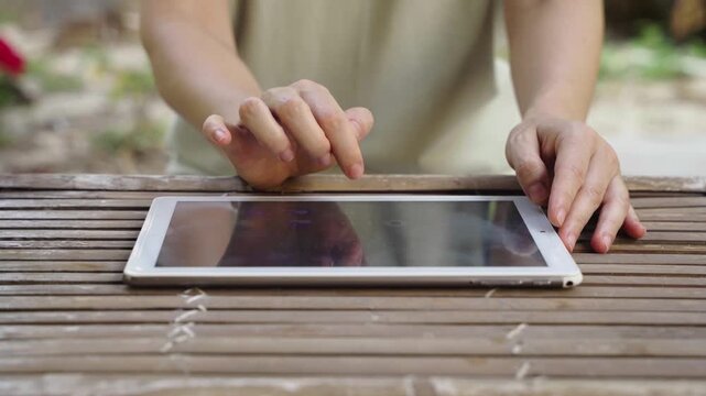 Person using tablet outdoors at wooden table, remote work in natural setting