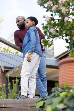 African American father and son standing on deck leaning on cable railing, son wearing denim shirt