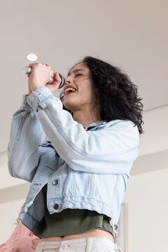 Female singer singing into handheld microphone, holding it, wearing denim jacket in rehearsal room