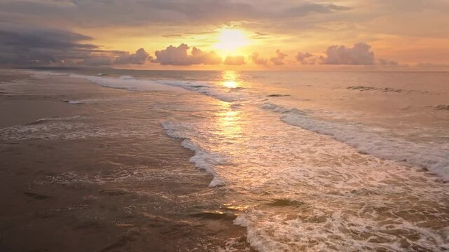 Golden sunset sun over Green Bowl Beach, Bali. Warm light reflecting on the Indian Ocean, foamy waves roll toward shore beneath a dramatic bright colorful sky. Natural background. Aerial drone flight