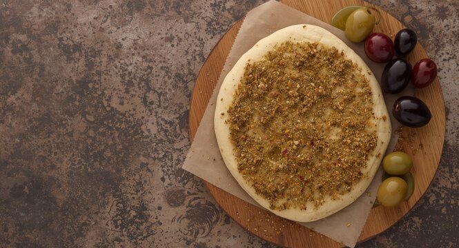 Top view of zaatar manakeesh on rustic wooden board with olives and olive oil featuring copy space