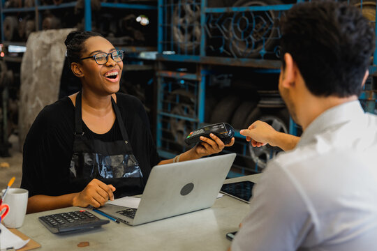 Female mechanic processing card payment with customer at auto repair shop counter