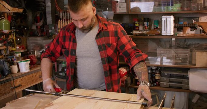 Carpenter work. Furniture making. Man tightening professional bar clamp on wooden panel set in joinery workshop interior for diy project.