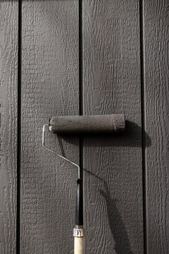 A paint roller leaning up against a freshly painted barn wall in the sunshine.