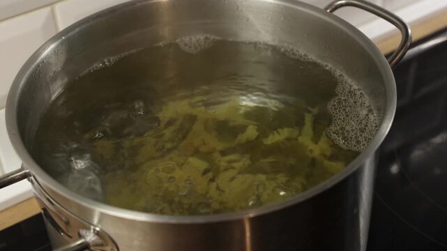 Adding dry two colors Italian pasta into boiling water in stainless steel pot during cooking process.